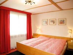 Ein Schlafzimmer mit einem hölzernen Bett, roten Vorhängen und drei gerahmten Bildern an der Wand.