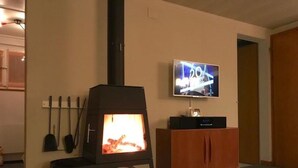 Een woonkamer met een houtkachel, een aan de muur bevestigde televisie en een houten kast.