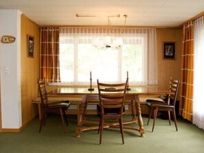 A dining area with a long table and chairs, a chandelier, and a window with curtains. - Pony 5-Bettwohnung Appartement/Fewo, Dusche oder Bad, WC, 2 Schlafräume by Interhome (Lenk)