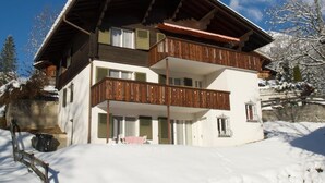 Een chalet met twee verdiepingen, een houten balkon en een met sneeuw bedekte dak.