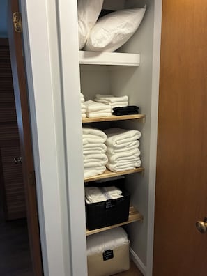 Ein Schrank mit Regalen, voll mit gefalteten Handtüchern und einer schwarzen Aufbewahrungsbox.
