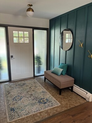 Ein Zimmer mit einer beigefarbenen Bank, einem gemusterten Teppich, einer Tür mit Fenster und einem wandmontierten Spiegel.