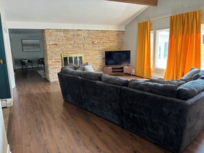Ein modernes Wohnzimmer mit einer großen Eckcouch, einem Flachbildfernseher und einer Steinwand.