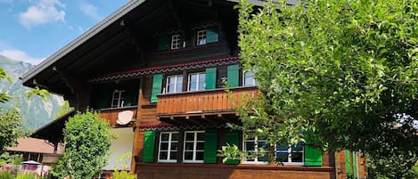 Un immeuble à plusieurs étages, doté d’un toit en pente, de balcons en bois et de volets verts.
