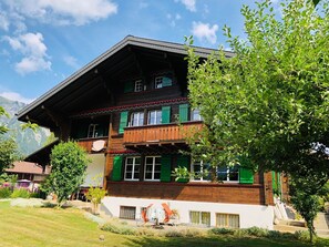 Ein mehrstöckiges Gebäude mit einem geneigten Dach, Holzbalkonen und grünen Fensterläden.