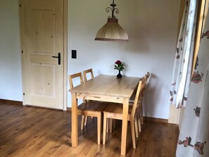 Ein Holztisch mit Stühlen, eine Vase mit Blumen, eine Pendelleuchte und eine Tür.
