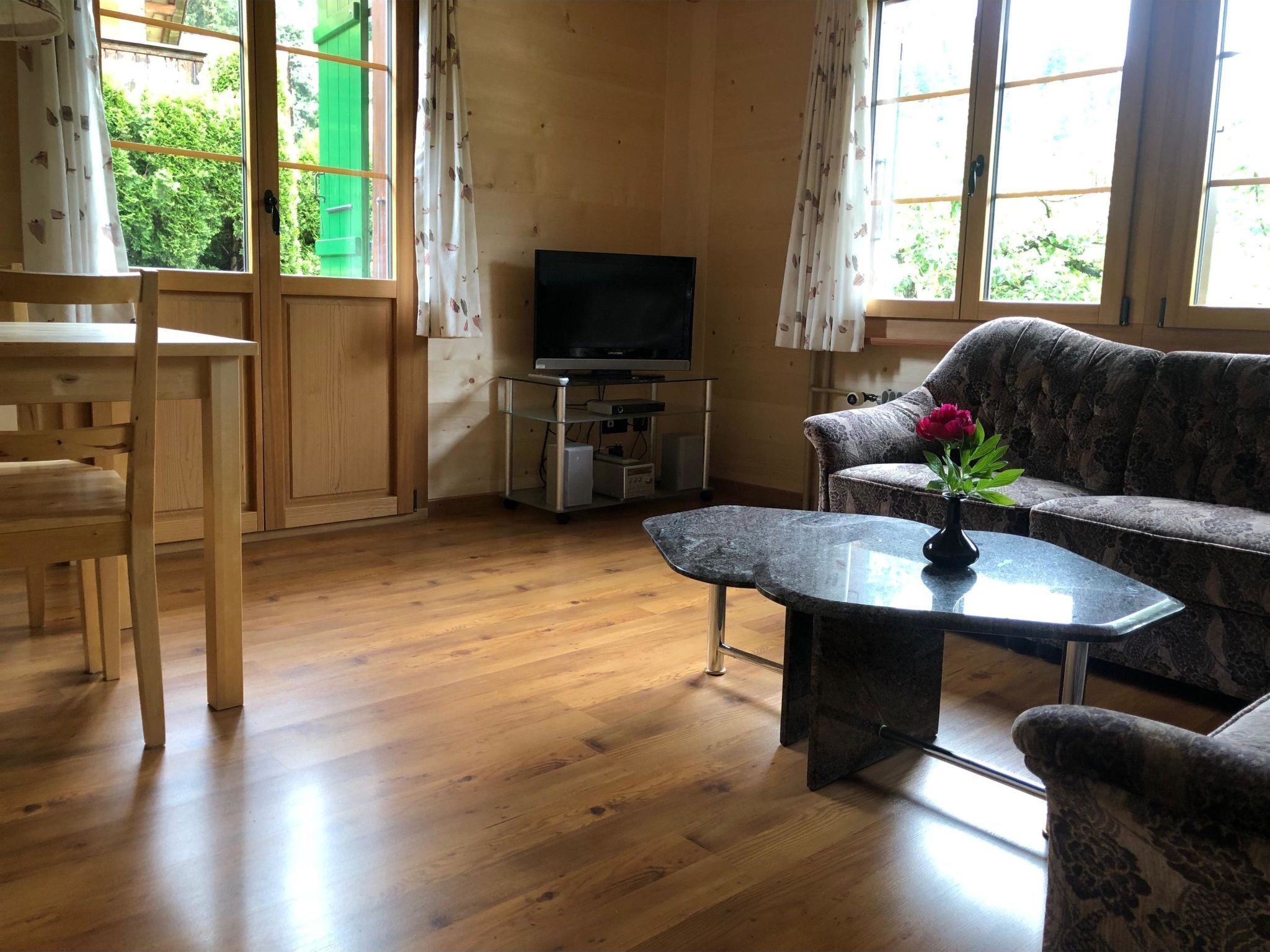 A living room with a wooden floor, a sofa, a coffee table, a TV, and a window with curtains.