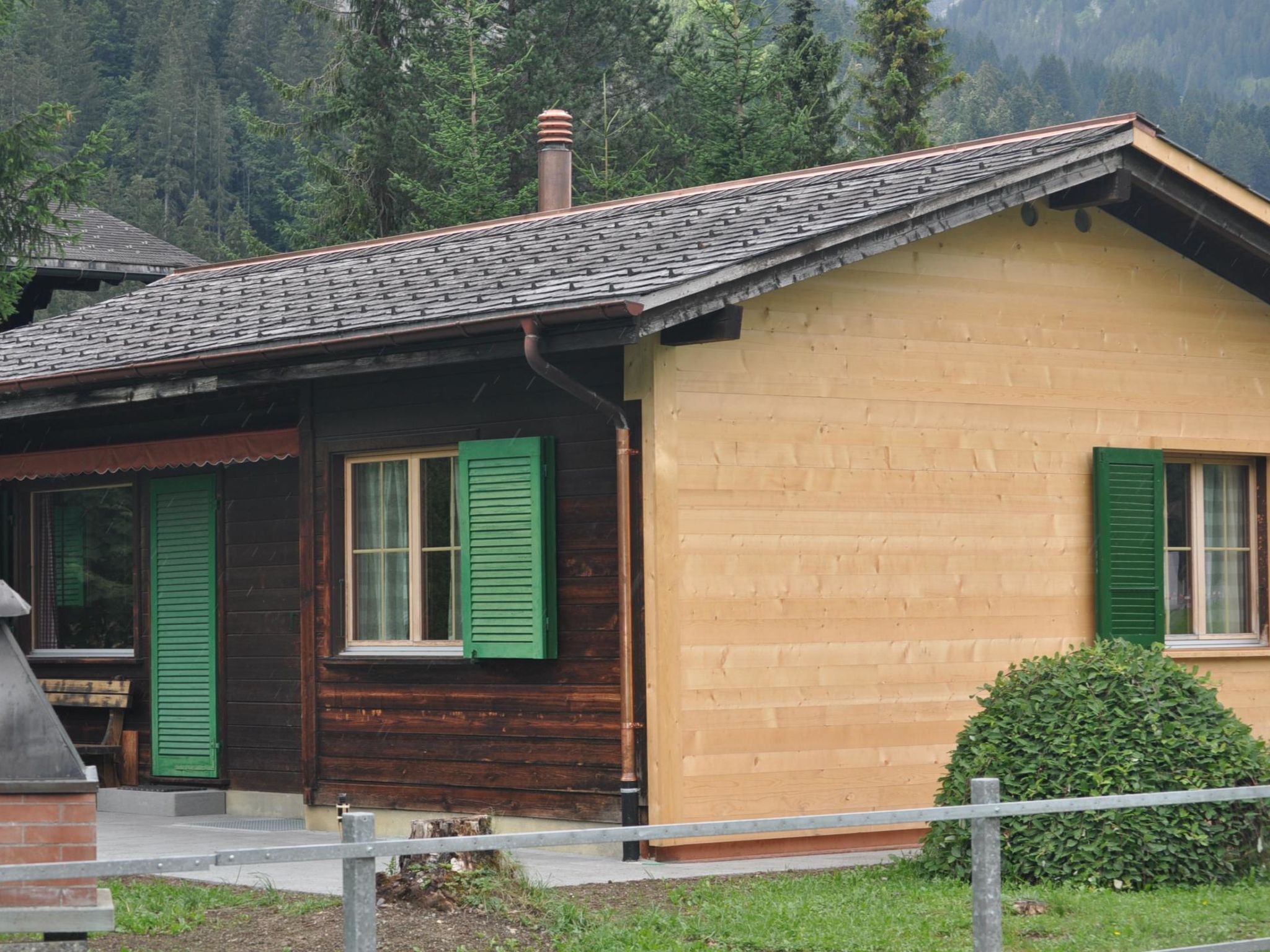 Ein zweigeschossiges Holzhaus mit grünen Fensterläden, einem Schornstein und einer kleinen Veranda.
