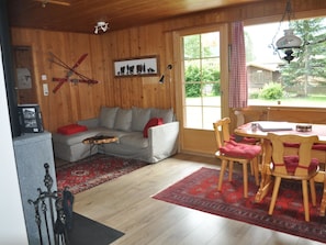 Ein gemütliches Zimmer mit Holzeinrichtung, einer Couch, einem Esstisch mit Stühlen und Blick ins Freie.