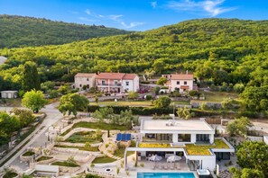 A modern villa with a swimming pool, surrounded by lush greenery and hills.