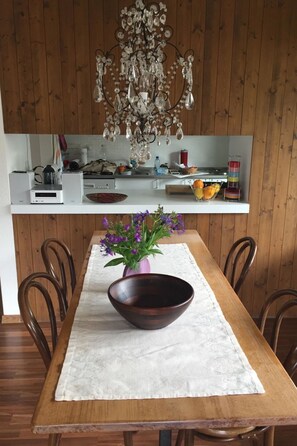 Ein Holztisch mit einer dunklen Schale in der Mitte und einer violetten Vase mit Blumen.