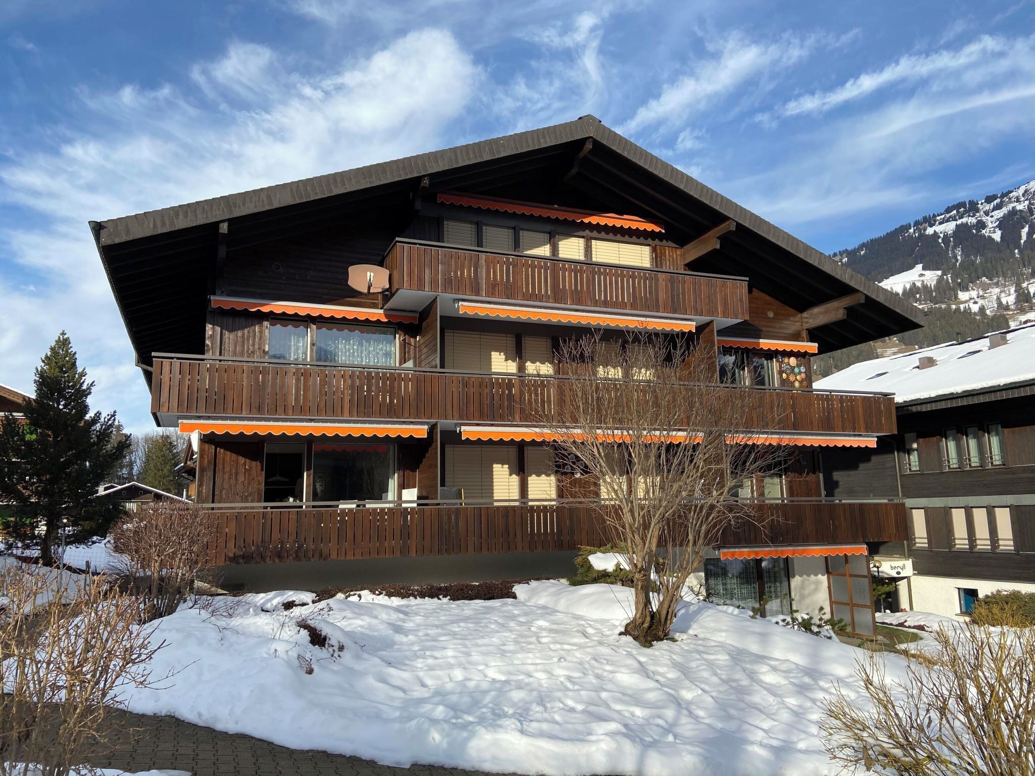 A multi-story building with balconies, a ski slope in the background, and a clear sky.