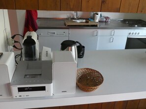 Eine Küche mit weißer Arbeitsplatte, einer Kaffeemaschine, einem Wasserkocher und einem Korb.