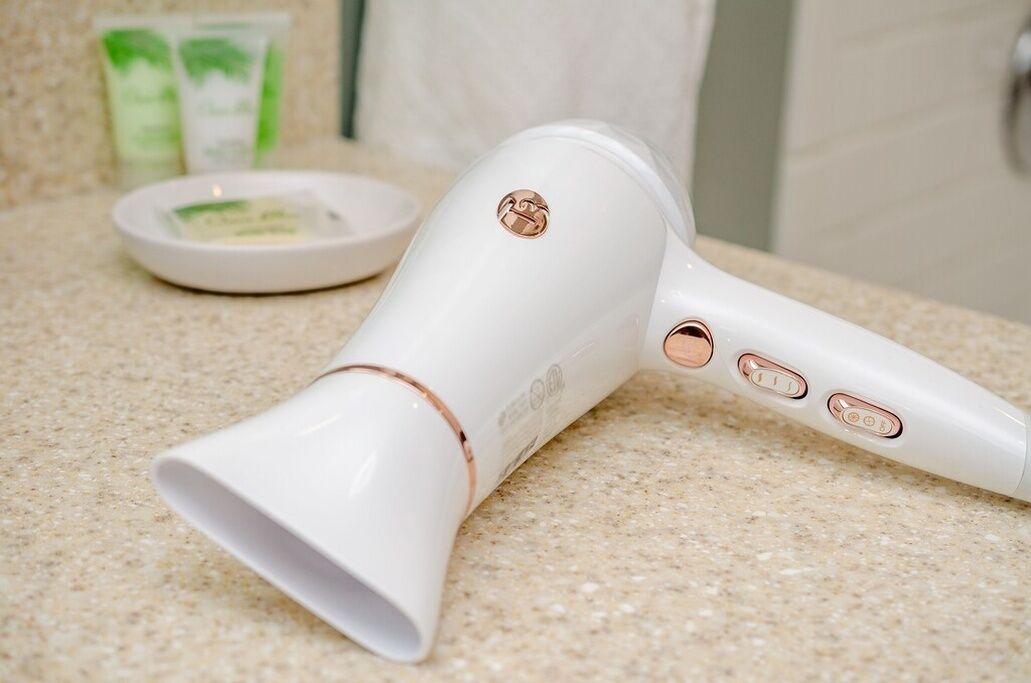 A white hair dryer with rose gold accents on a countertop.