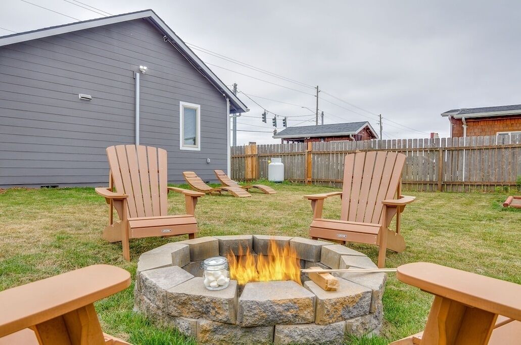 Un patio trasero con un hogar a leña de piedra, dos sillas Adirondack y una mesa de madera.