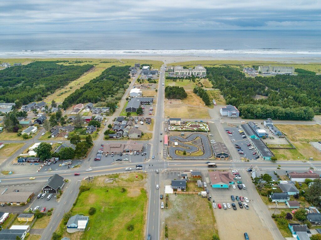 Vista aérea de un pueblo costero con una carretera principal, zonas de estacionamiento y edificios.