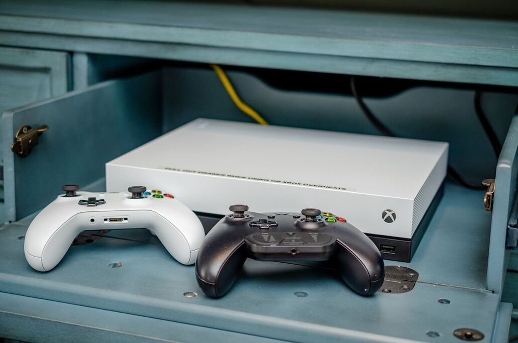 A white Xbox console with a black controller on a blue surface.