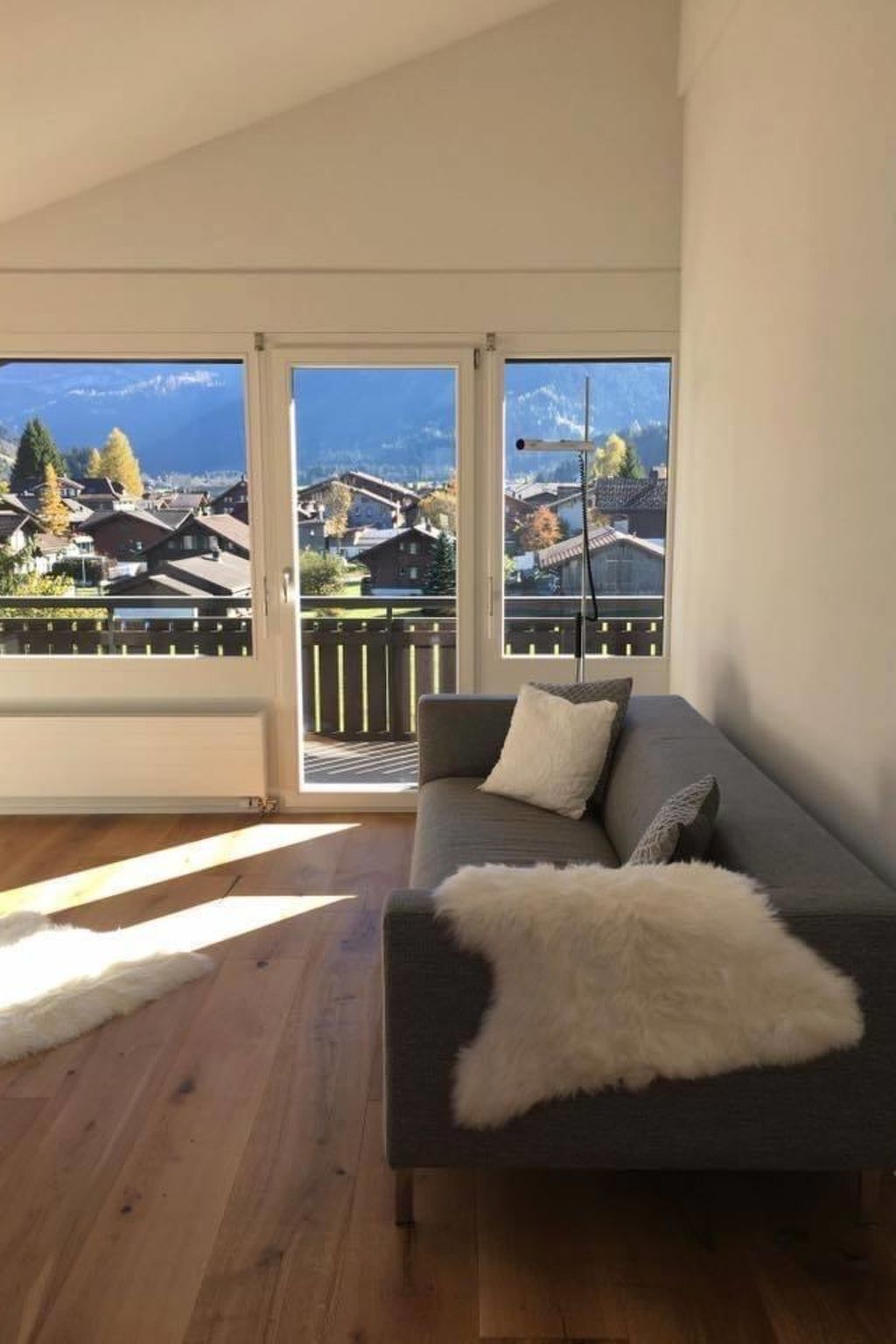 Ein Zimmer mit einer Couch, einer weißen, flauschigen Decke und Blick auf Häuser durch große Fenster.