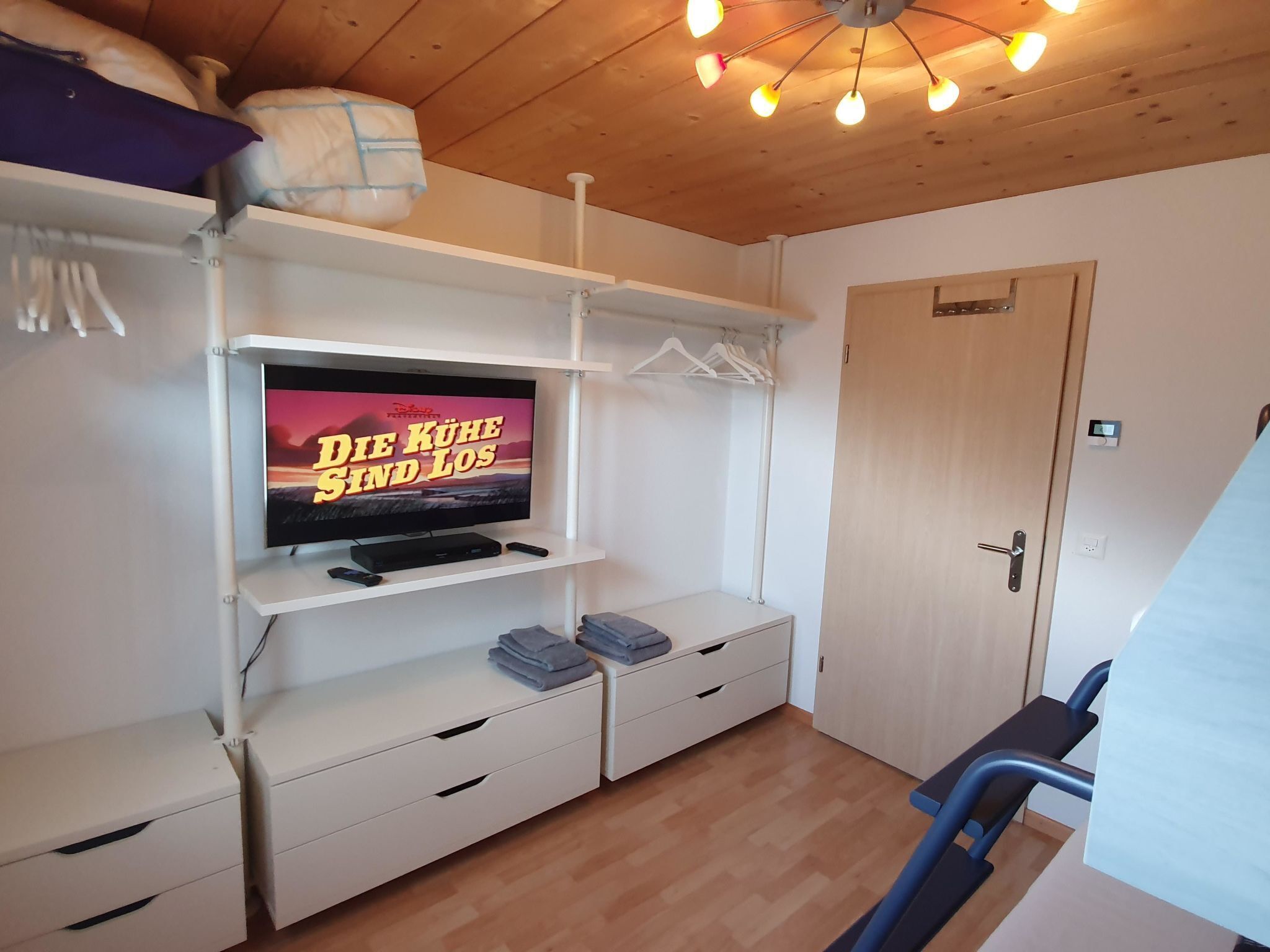A room with a television on a white shelf, a door, and a ceiling light fixture.