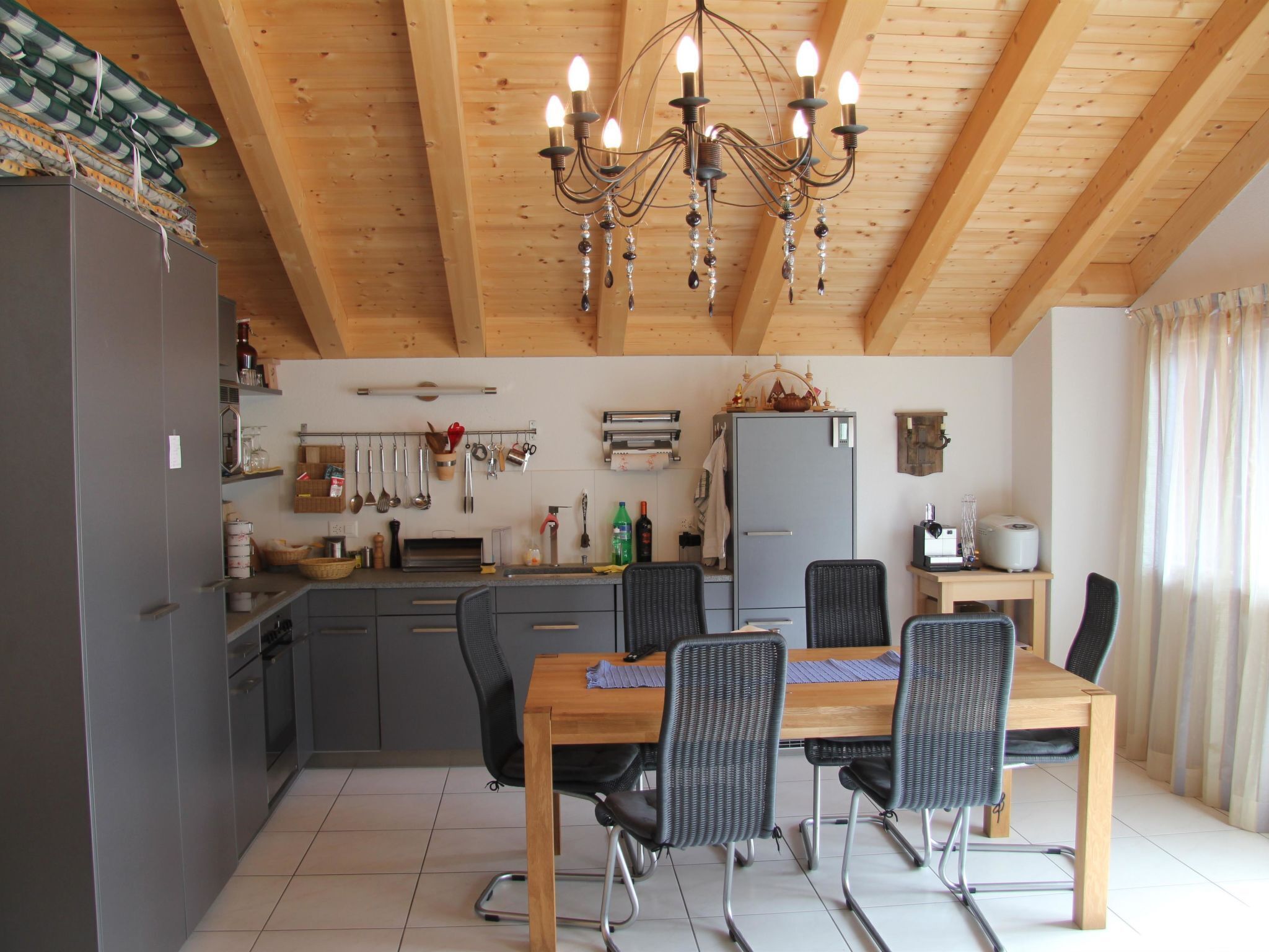 Eine moderne Küche mit Holzbalken, einer Chandelieber und einem Essbereich mit Stühlen und einem Tisch.
