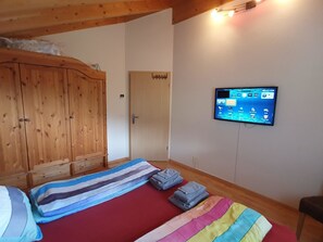 Una habitación con una cama, un armario de madera, un televisor fijado a la pared y una puerta.