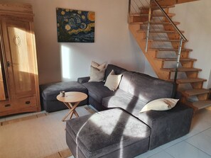 Ein Wohnzimmer mit grauem Sofa, einem kleinen Holztisch, einem Gemälde an der Wand und einer Holztreppe.
