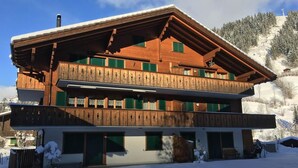 Eine zweistöckige Holzhütte mit Balkon, vor einer verschneiten Berglandschaft gelegen.