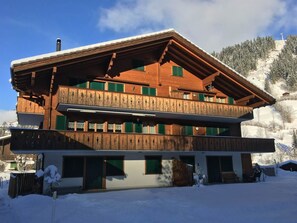 Eine zweistöckige Holzhütte mit Balkon, vor einer verschneiten Berglandschaft gelegen.