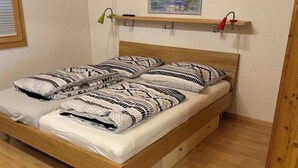 Ein Einzelbett mit gemusterten Textilien, ein Holzkopfende, ein Nachttisch mit Lampe und ein Bild an der Wand.