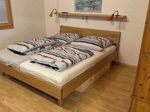 Ein Einzelbett mit gemusterten Textilien, ein Holzkopfende, ein Nachttisch mit Lampe und ein Bild an der Wand.