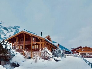 Eine Holzhütte mit geneigtem Dach, umgeben von schneebedeckten Bäumen und Bergen.