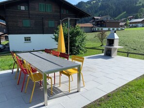 En uteplats med ett bord och stolar, en grill och utsikt över ett berg.
