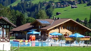 Un hôtel doté d’un espace piscine, comprenant des chaises longues et des parasols, le tout situé dans un cadre magnifique, avec des collines verdoyantes et des montagnes boisées en arrière-plan.