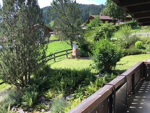 A wooden deck overlooking a lush garden with ferns and a wooden fence, with houses and a mountain in the background. - Chriba Appartement/Fewo, Dusche oder Bad, WC, 3 Schlafräume 6-Bett-Wohnung by Interhome (Lenk)