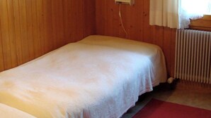 En enkeltseng i et rum med trævægge, en radiator og et vindue med gardiner.