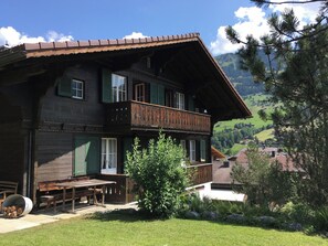 Ein zweistöckiges Holzhaus mit einem Balkon, einem Holztisch und einem Stuhl draußen.