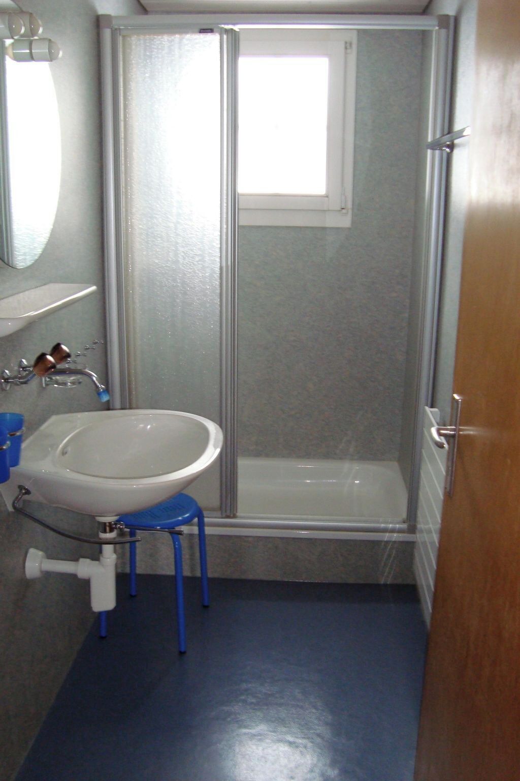 Une salle de bain avec un lavabo blanc, une cabine de douche en verre et une petite fenêtre.