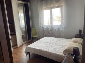A bedroom with a bed, a chair, a wardrobe, and a window with curtains. - SIM NOR Vacation Home… RELAX Three-Room Apartment (Budoni)