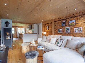 A modern living room with a wooden ceiling, a white sofa, a fireplace, and a dining area with a view. - Chalet Bijou+ 1 OG Appartement/Fewo, Dusche, WC, 2 Schlafräume by Interhome (Lenk)