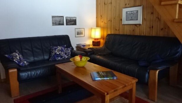 Ett vardagsrum med en svart lädersoffa, ett soffbord i trä och en lampa.