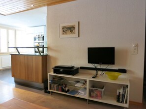 Ein modernes Wohnzimmer mit einem Flachbildfernseher, einem Holzschrank und einem Bücherregal voller Bücher und Zeitschriften.