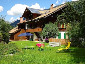 A wooden house with a sloped roof, a balcony, and a small garden with lawn chairs and a table. - Lischenhaus - Strubel Appartement/Fewo, Dusche oder Bad, WC, 2 Schlafräume by Interhome (Lenk)
