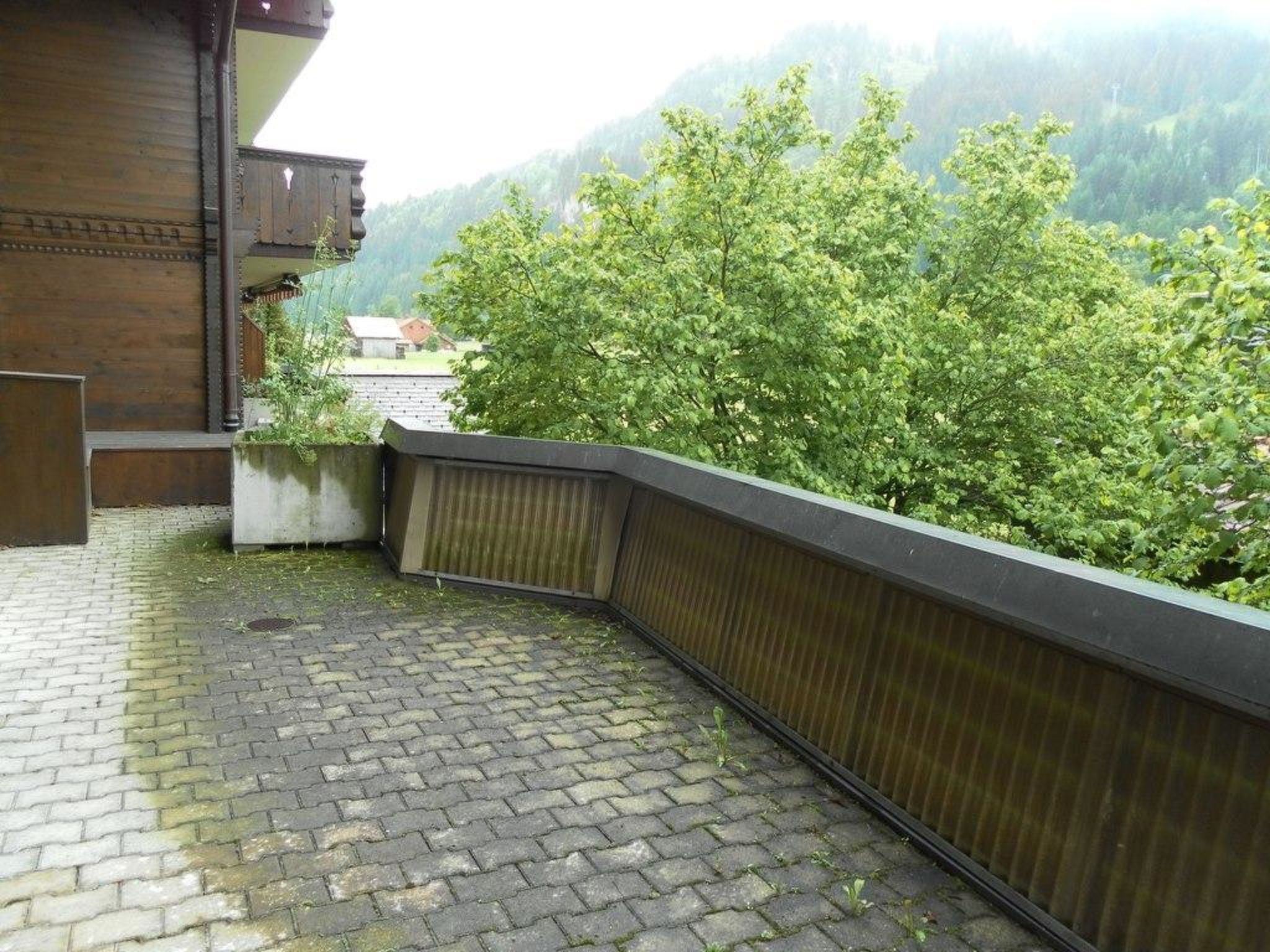 A stone-paved balcony with a metal railing overlooking a forested hillside.