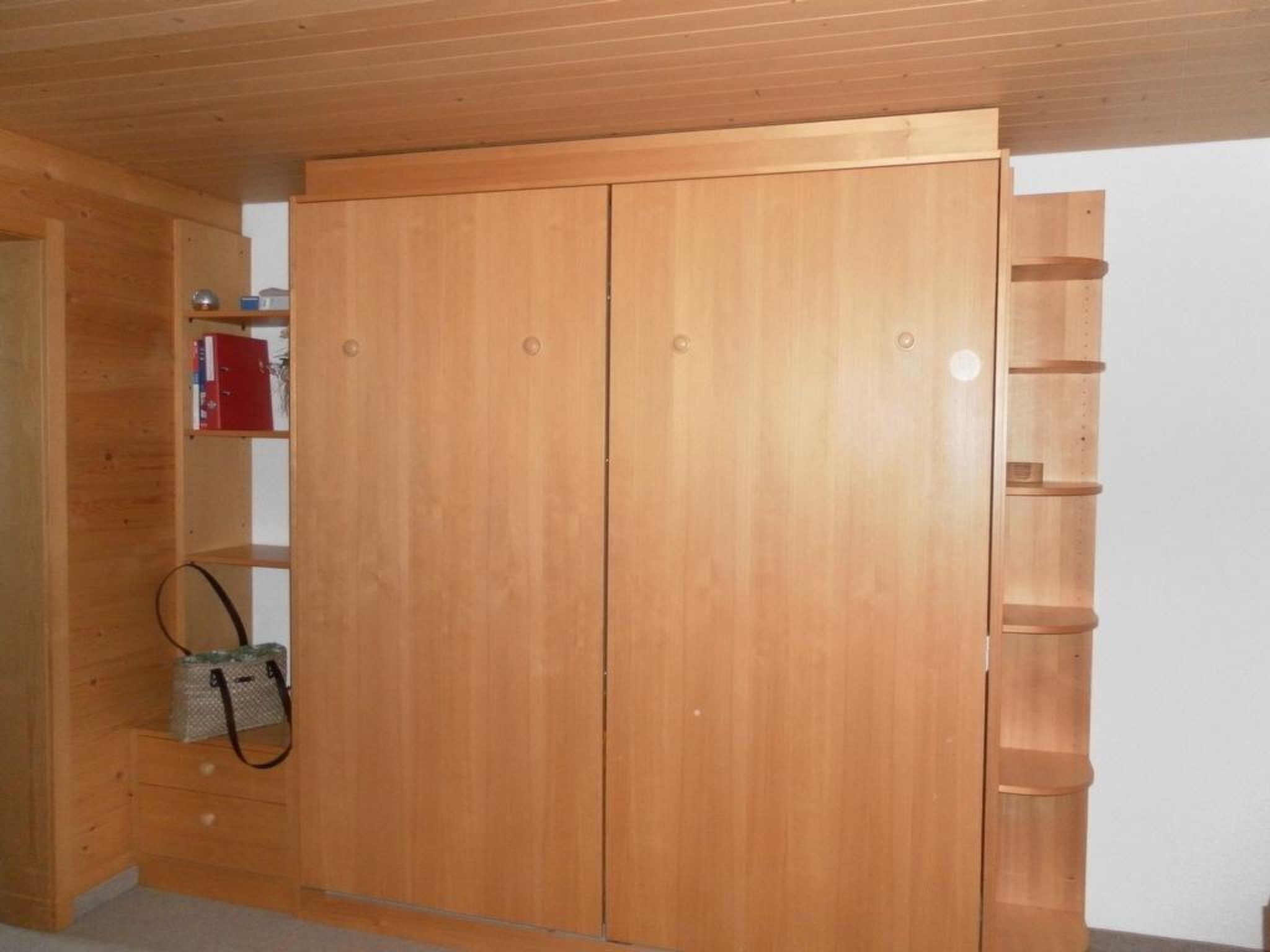 A wooden wardrobe with a shelf on the left and a hanging rack on the right.