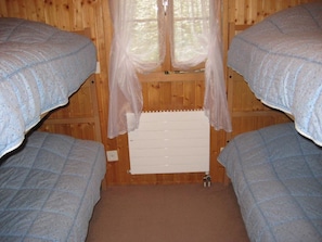 A room with two beds, a radiator, and a window with sheer curtains.