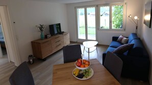 Ett modernt vardagsrum med ett matbord i trä, en blå soffa och en tv som står på ett träskåp.