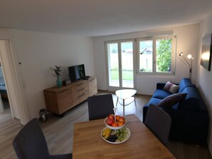 A modern living room with a wooden dining table, a blue sofa, and a television on a wooden cabinet. - Chalet Claudia Appartement/Fewo, Dusche, 1 Schlafraum 2-Bett-Wohnung by Interhome (Lenk)