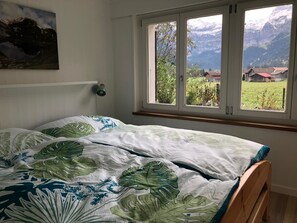 A bedroom with a bed, a window with a view of mountains, and a wall-mounted lamp. - Chalet Claudia Appartement/Fewo, Dusche, 1 Schlafraum 2-Bett-Wohnung by Interhome (Lenk)