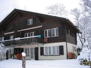 A two-story wooden building with a balcony and a snow-covered roof. - Chalet Claudia Appartement/Fewo, Dusche, 1 Schlafraum 2-Bett-Wohnung by Interhome (Lenk)