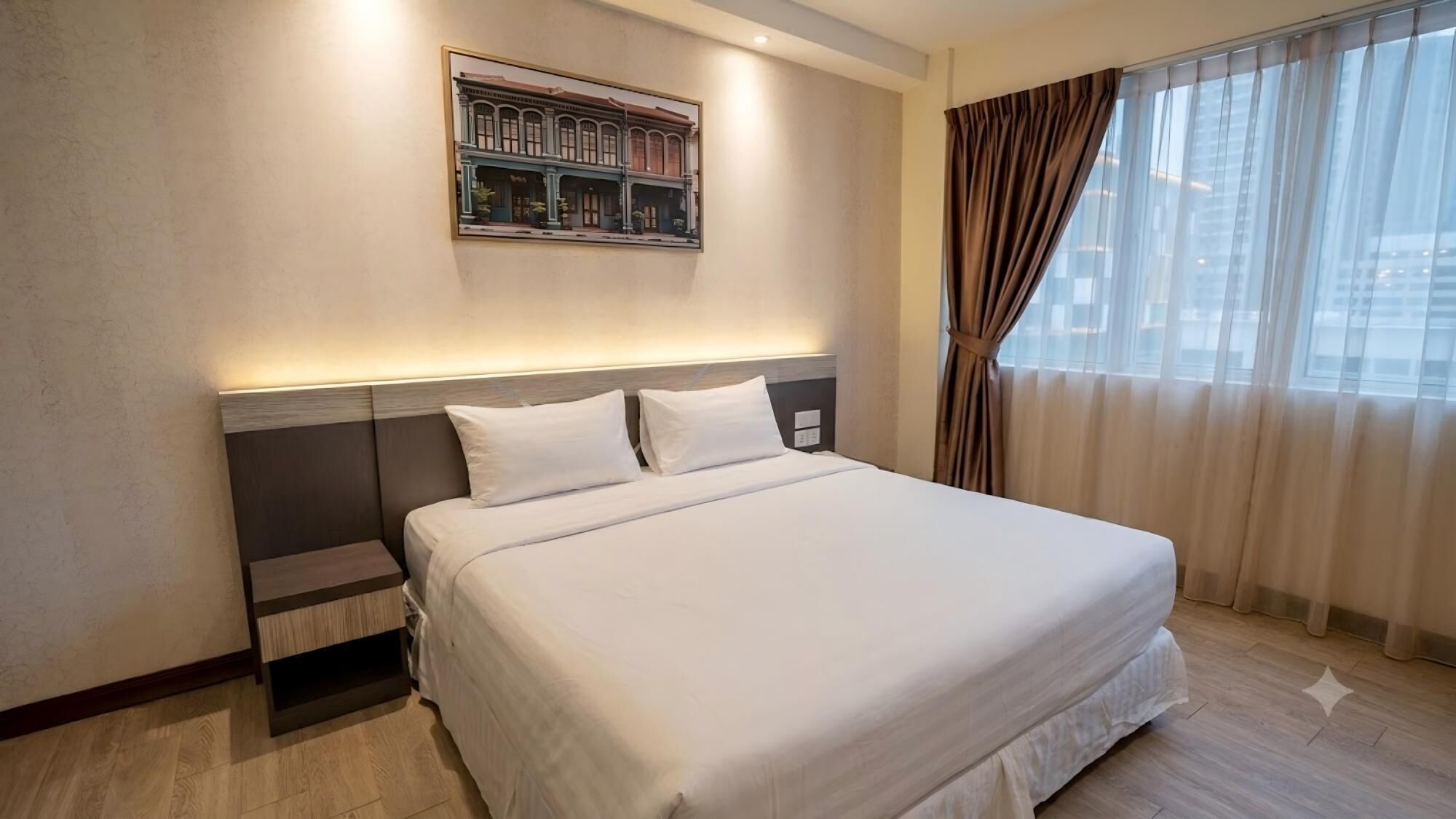 A hotel room with a large bed, a nightstand, a wall-mounted artwork, and a window with curtains.